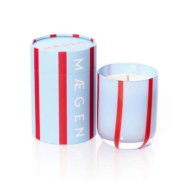 Candle with striped design and 'Mégen' branding on a white background