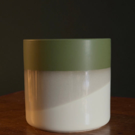A ceramic vase with a green and white color blocking design on a wooden surface.