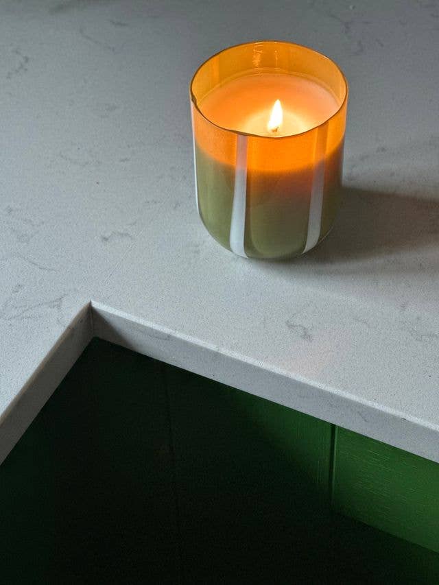 Candle in an orange glass holder on a white surface