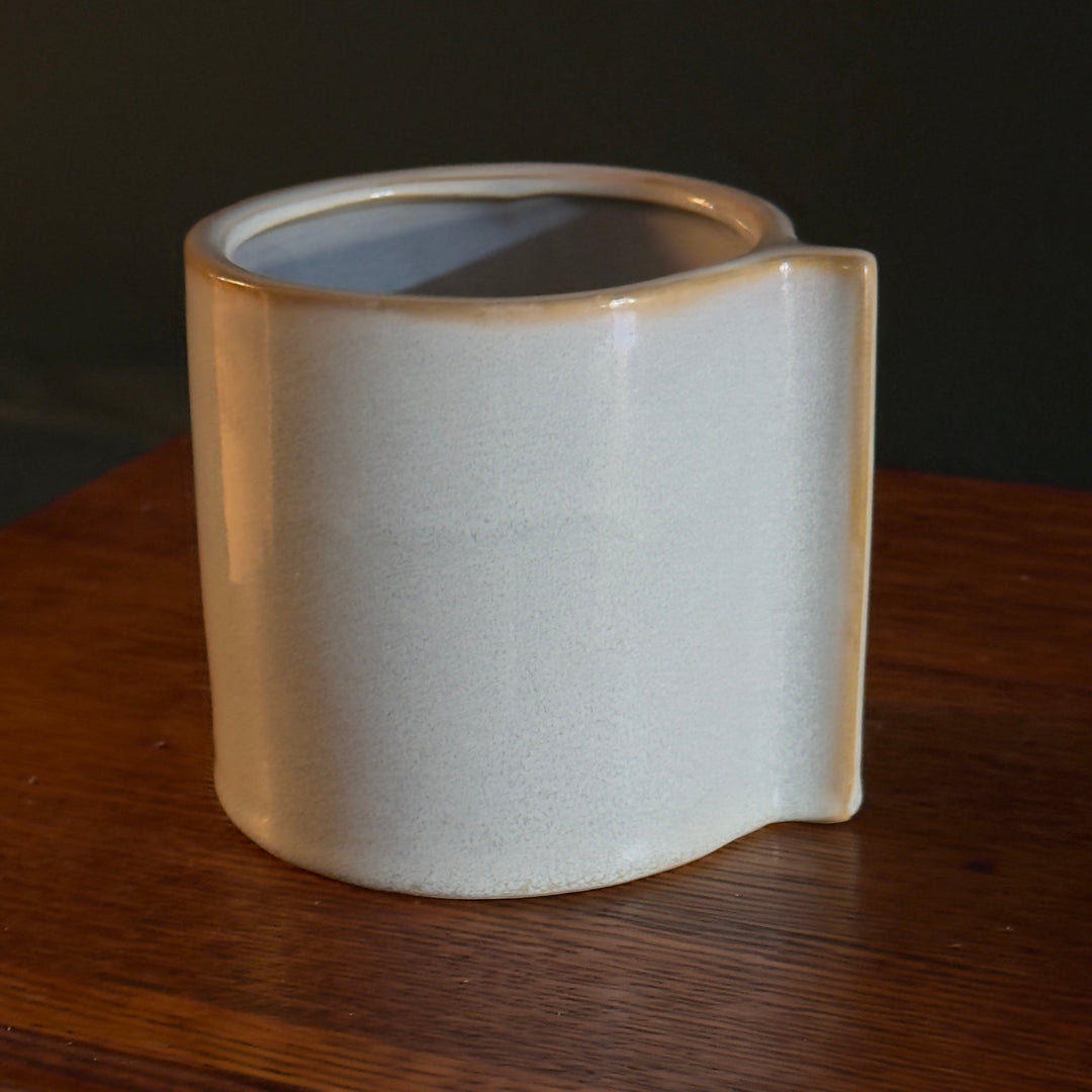 A beige and blue ceramic planter or vase with a modern abstract design on a wooden surface.