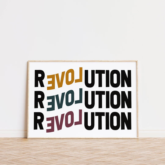 A framed print with the word 'REVOLUTION' repeated in a pattern, displayed leaning against a wall with a radiator below it and a plant to the side.