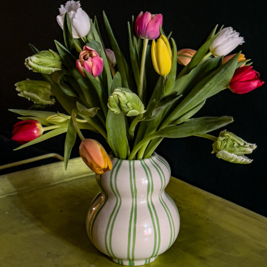 Off-white with green strip ceramic vase filled with multicolored tulips in white, yellow, red, purple, pink and light green.