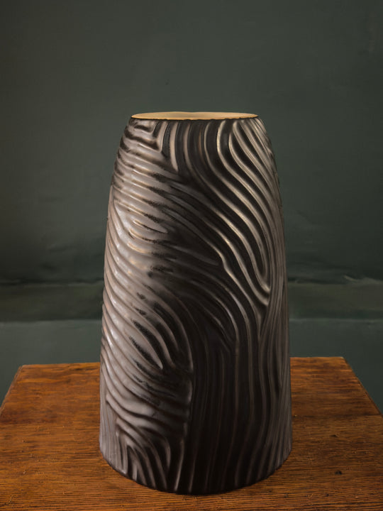 A matte black vase with a wave-like pattern displayed against a dark background.