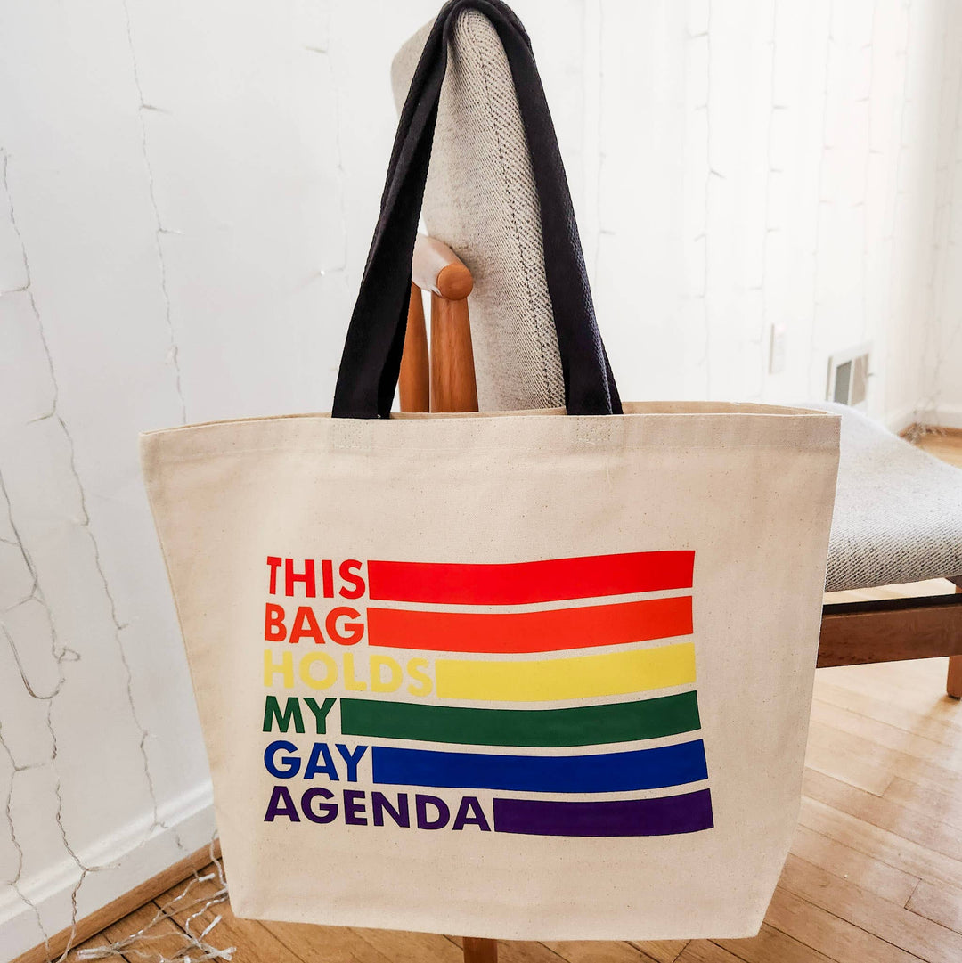 Tote bag with rainbow design and text on a chair against a white wall.