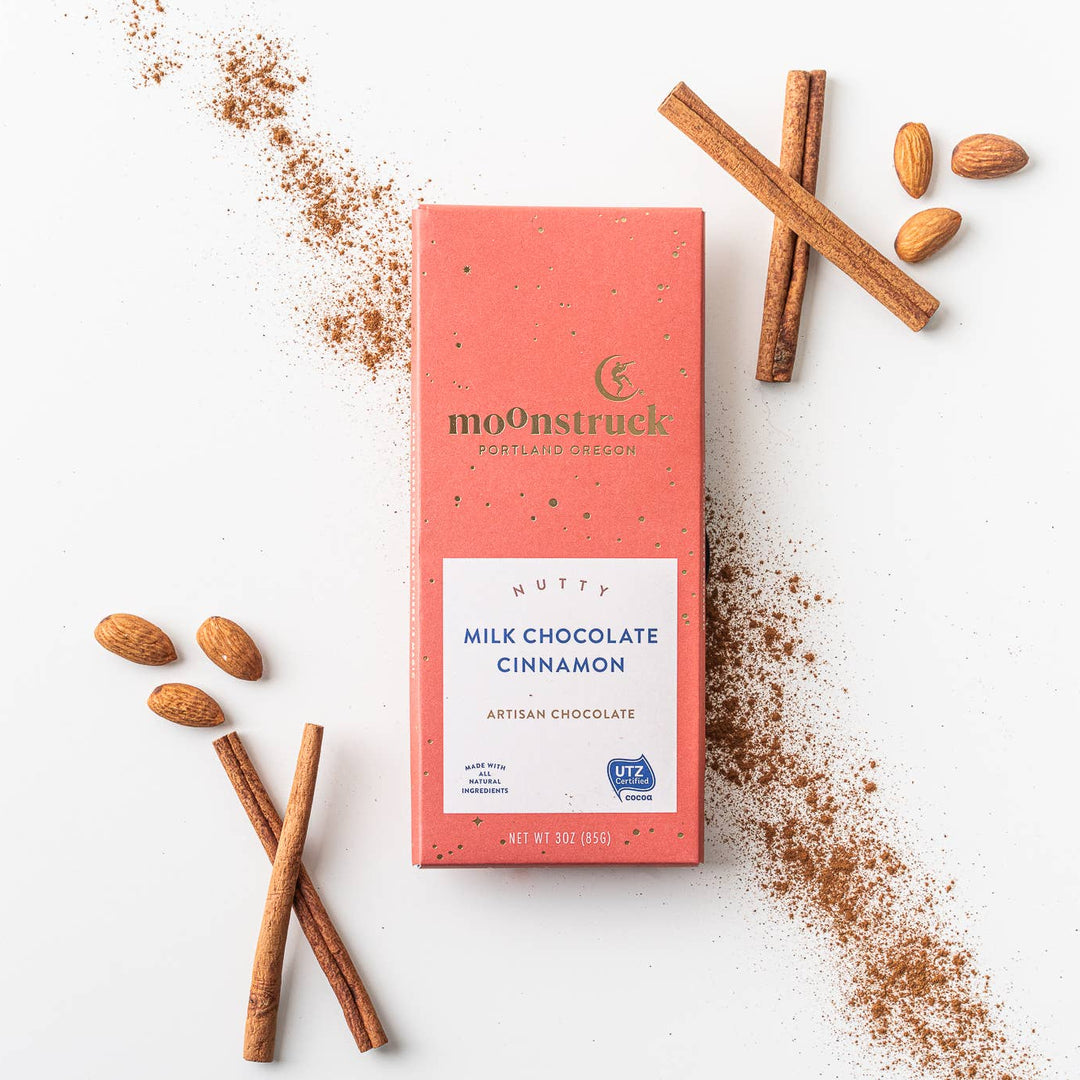 Moonstruck Milk Chocolate Cinnamon bar with cinnamon sticks and ground cinnamon on a white background
