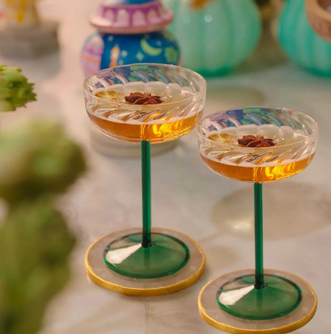 Elegant cocktail glasses with amber drinks and star anise garnish, set on marble with colorful decor.