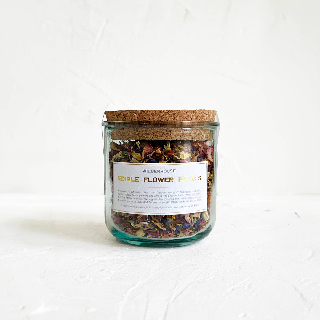 Glass jar with cork lid containing dried edible flower petals on a white background