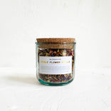 Glass jar with cork lid containing dried edible flower petals on a white background