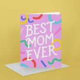 Greeting card with 'Best Mom Ever' text on a pink background with colorful shapes, on a yellow background.