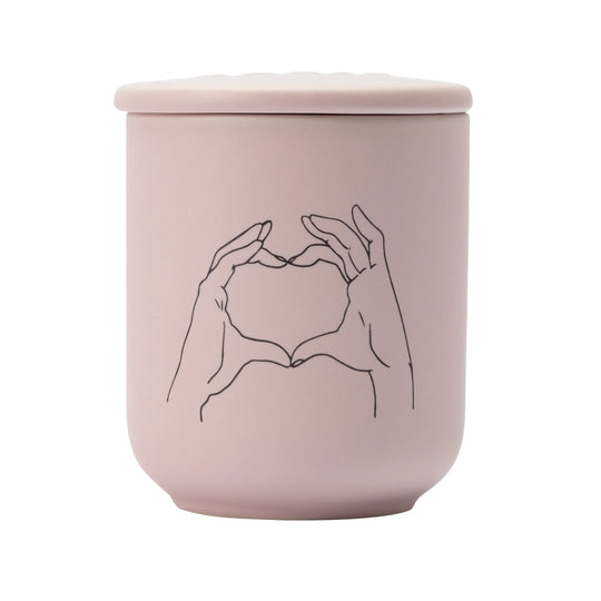 Pink ceramic jar with lid featuring a minimalist line drawing of hands holding a heart on a white background.