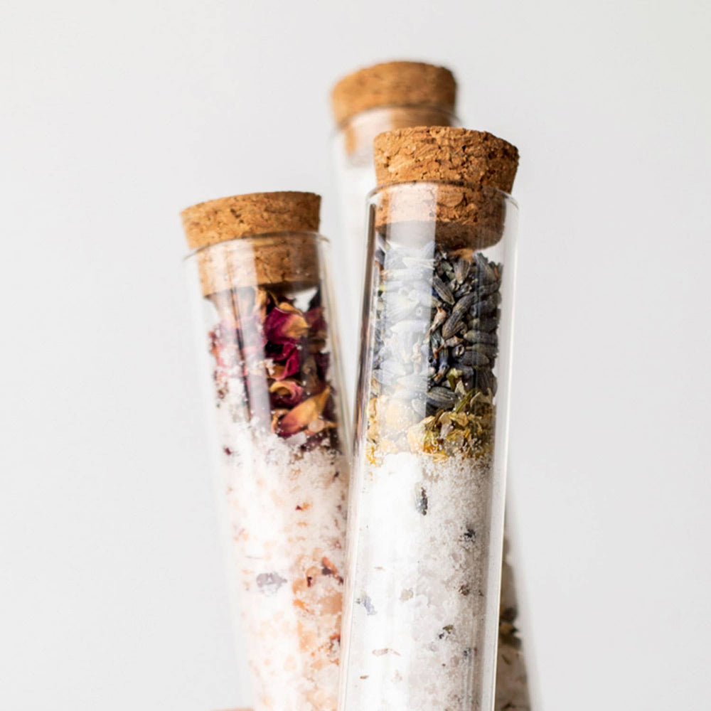 Three glass tubes with cork lids containing various dried herbs and salts on a light background