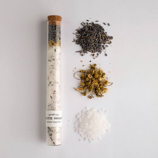 Shea butter bath soak tube with dried herbs on a light gray background