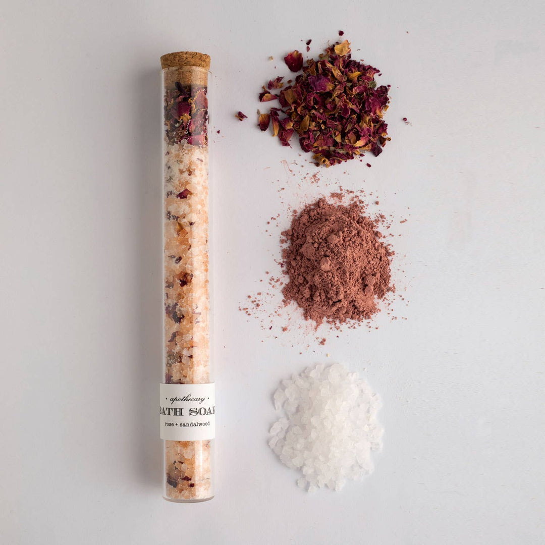 Tube of bath salts with rose petals and other ingredients on a light gray background