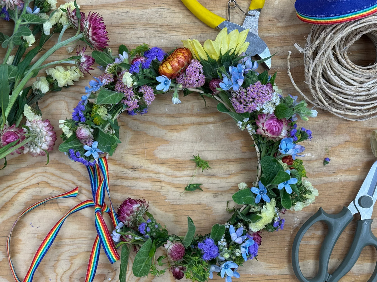 Colorful floral wreath with rainbow ribbon, fresh blooms, and tools on wooden surface
