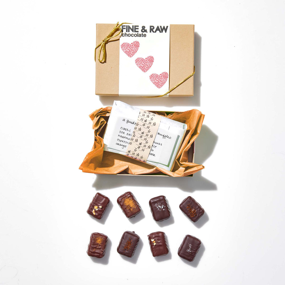 Box of Fine & Raw chocolate with a card and chocolate pieces on a white background
