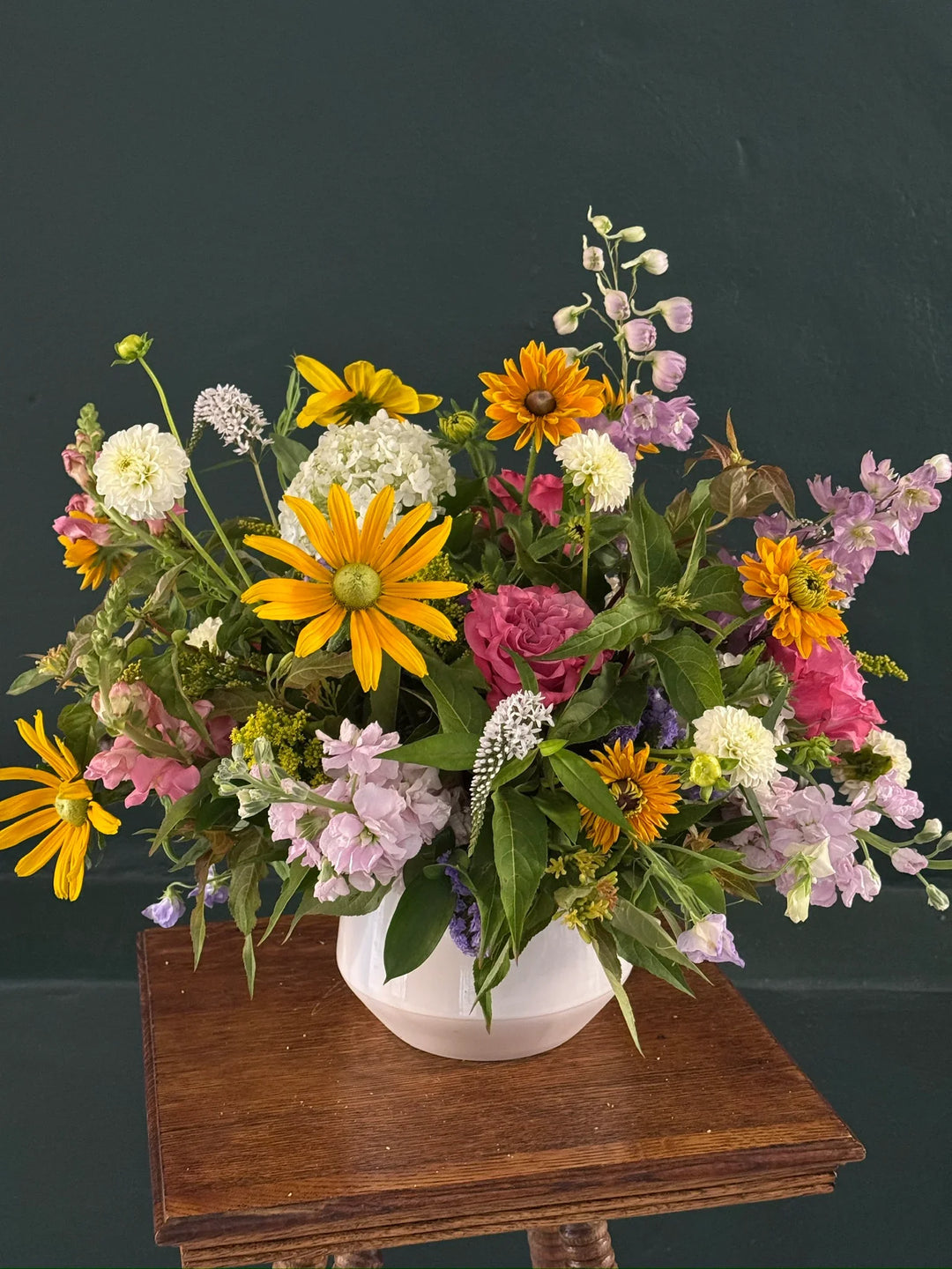 Vibrant floral arrangement with sunflowers, roses, and hydrangeas in a white vase on wooden table