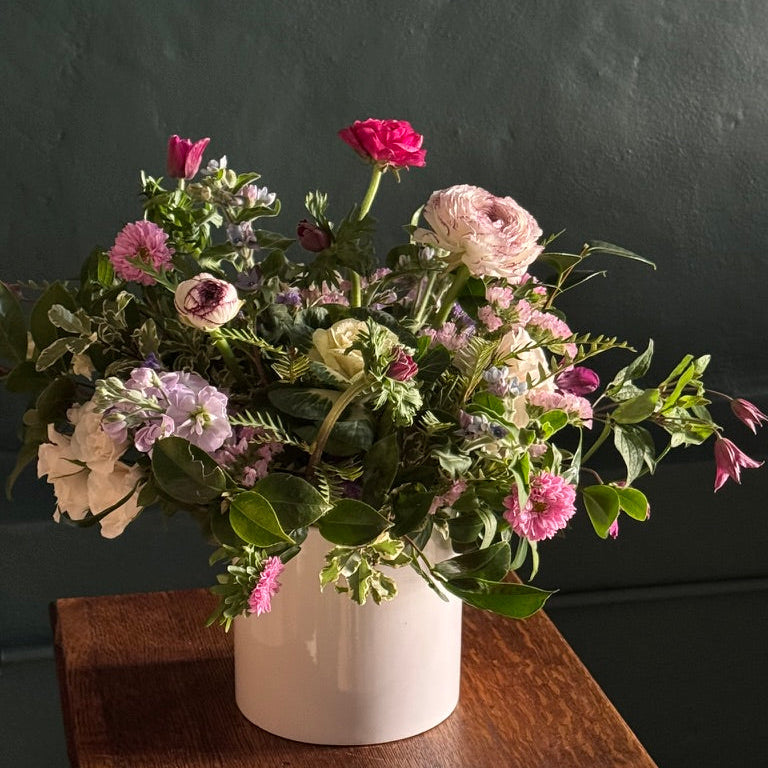 Bouquet of flowers in a white vase on a wooden surface with a dark background