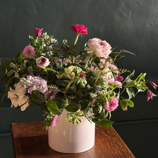Bouquet of flowers in a white vase on a wooden surface with a dark background