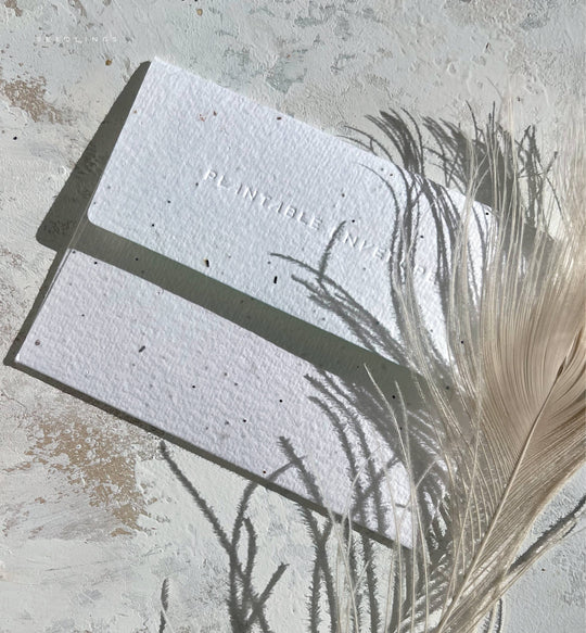 Seed paper card with 'Plantable' text on a textured surface with a feather.
