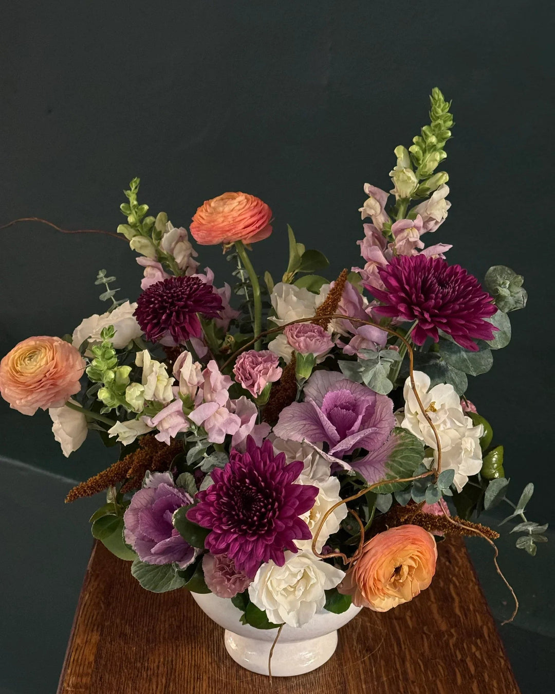 Vibrant floral arrangement with purple dahlias, peach ranunculus, and white blooms in a white vase