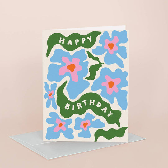 Birthday card with blue flowers, pink centers, and green leaves on a beige background