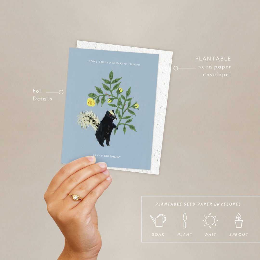 Hand holding a plantable seed paper envelope with bear and floral design on a beige background