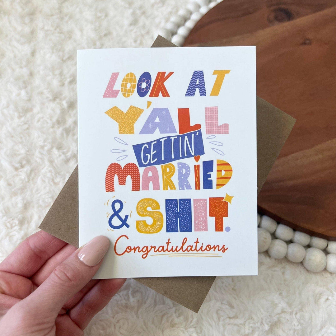 Hand holding a colorful wedding congratulations card with text on a textured surface.