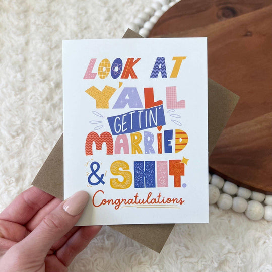Hand holding a colorful wedding congratulations card with text on a textured surface.
