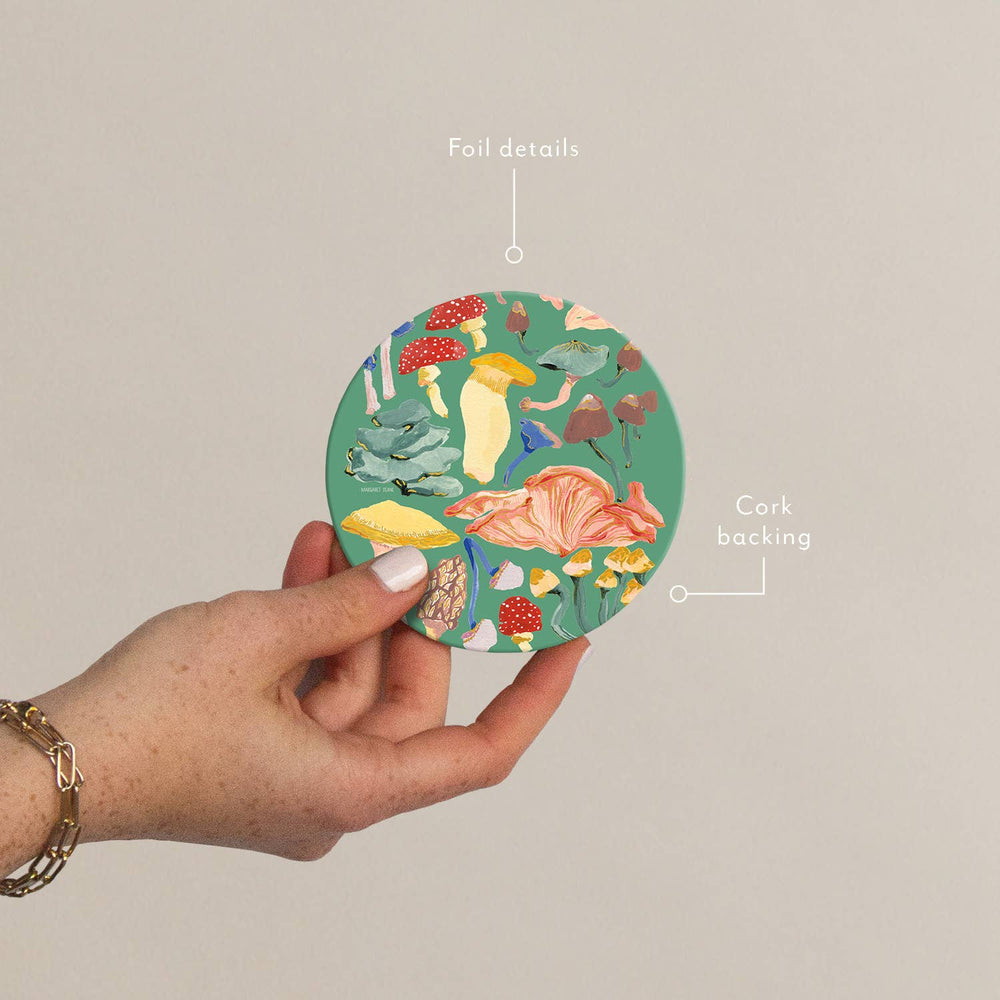 Hand holding a round, colorful coaster with nature-themed design on a beige background