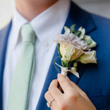 Person wearing a blue suit with a green tie and a floral boutonniere.