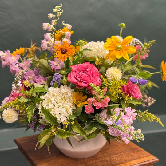 Colorful flower arrangement on a wooden stand with a dark background