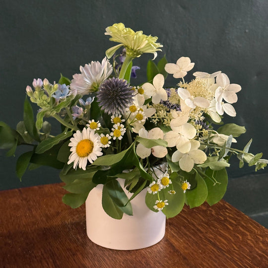 Bouquet of flowers in a white vase on a wooden surface with a dark background