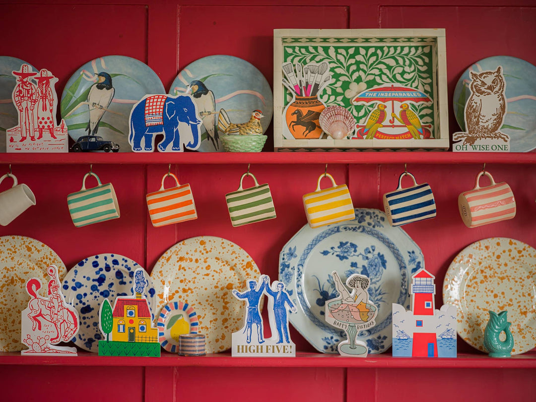 Collection of decorative plates, mugs, and a framed artwork on a red wall.