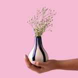 Hand holding striped vase with baby's breath flowers against pink background