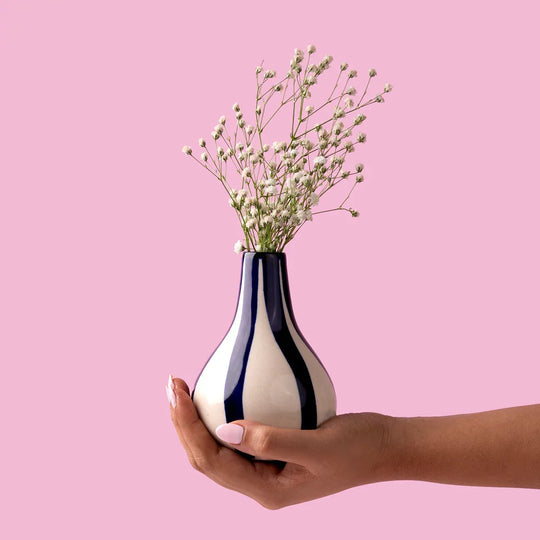 Hand holding striped vase with baby's breath flowers against pink background