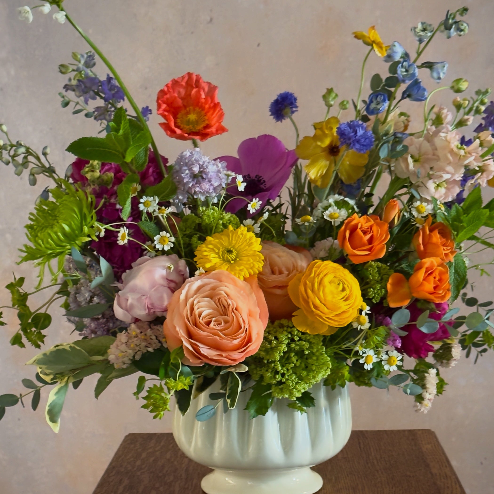 Colorful flower arrangement in a white vase on a wooden surface with a neutral background