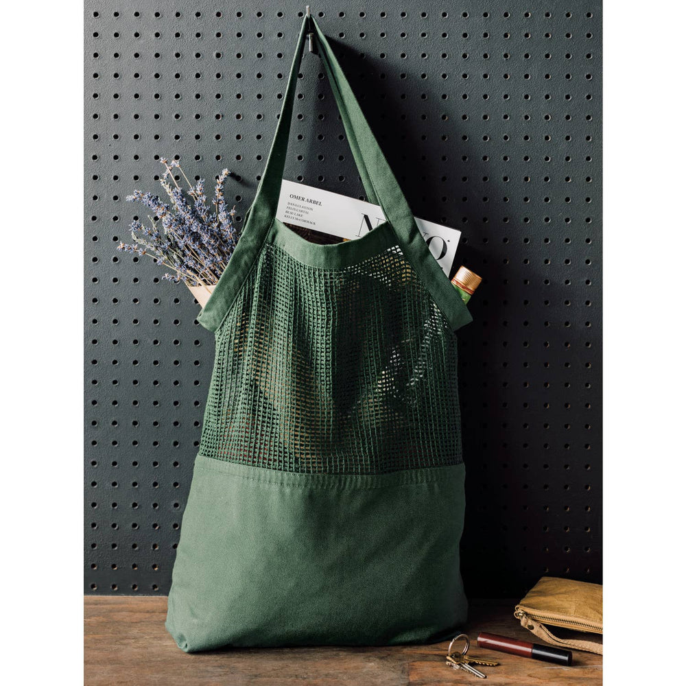 Green mesh tote bag with a wooden surface and pegboard background