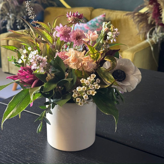 Floral arrangement in a white vase on a dark surface with a blurred background
