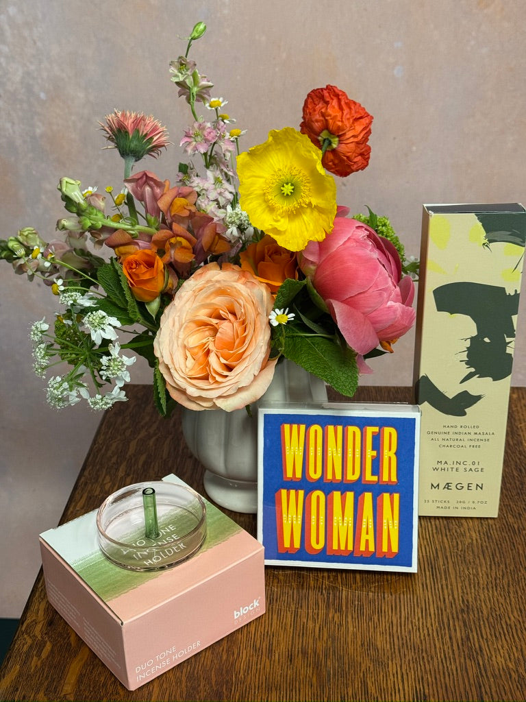 Bouquet of flowers, candle, and 'Wonder Woman' card on a wooden surface.