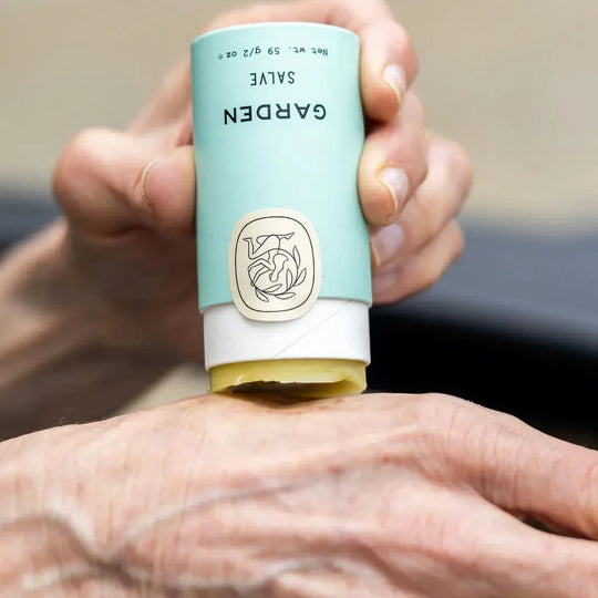 Hand applying salve from a blue and white tube labeled 'Garden' with a logo.
