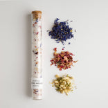 Tube of bath salts with dried flowers on a light gray background