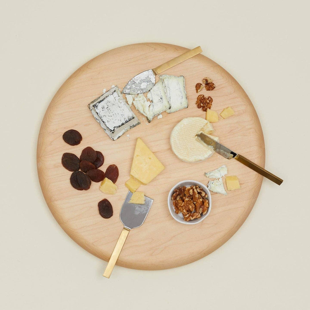 Wooden cheese board with assorted cheeses, dried apricots, walnuts, and gold-handled knives