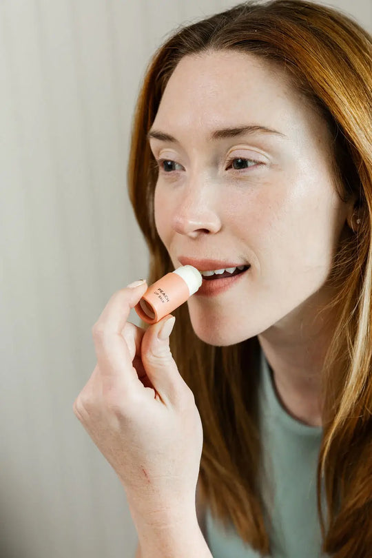 Woman applying lip balm to her lips with a neutral background