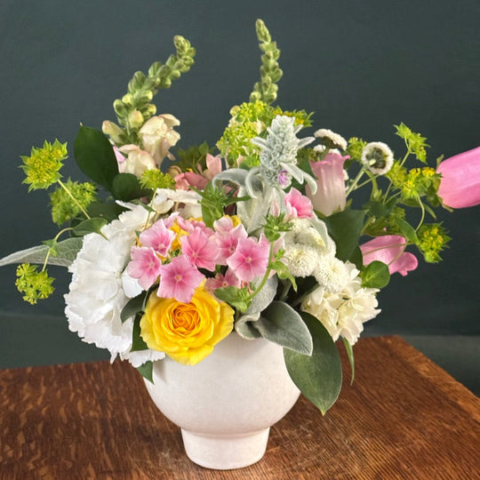 Floral arrangement in a white vase on a wooden surface with a dark background