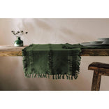 Green textured tablecloth on a wooden table with a vase and plates in the background.