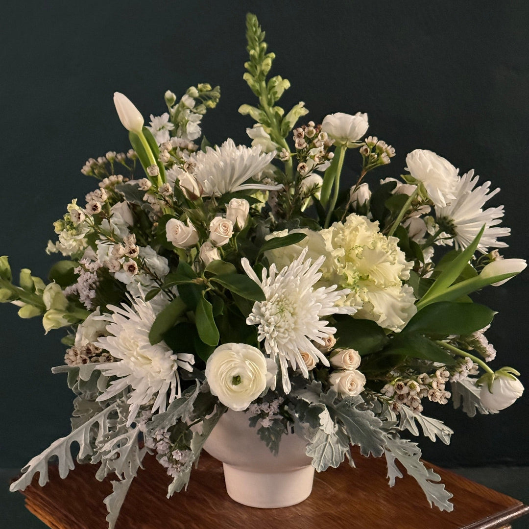 floral table centerpiece made up of white flowers and green and grey green foliage.