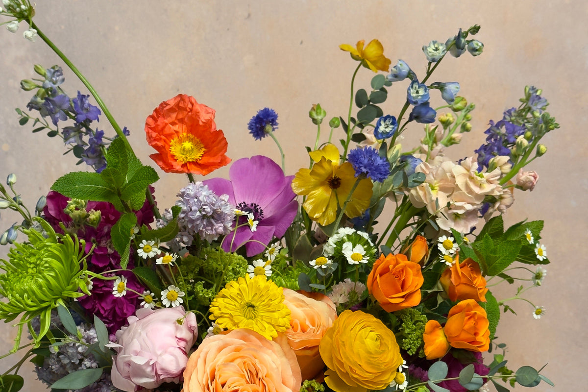 Colorful flower arrangement with a candle and box of chocolate on a wooden surface