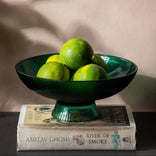 Green bowl with limes on top of books against a beige wall