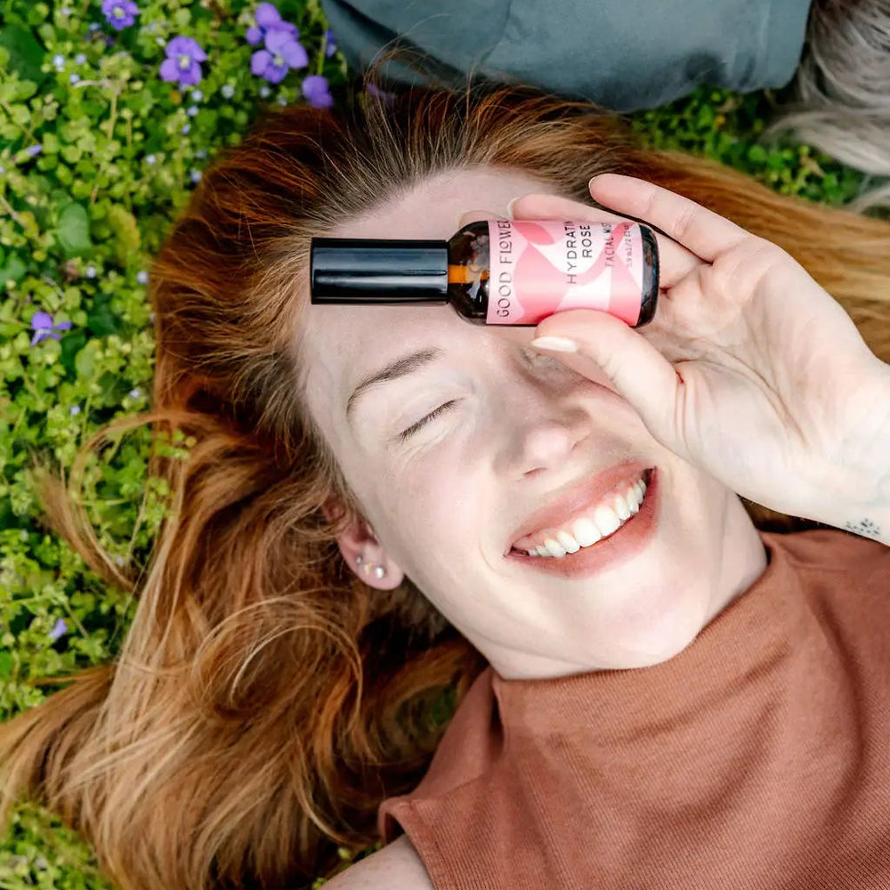 Person lying on grass holding a bottle of nail polish to their face