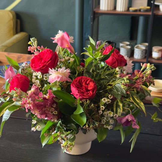 Bouquet of red and pink flowers in a white vase on a dark surface with a blurred background.